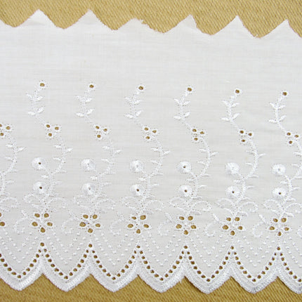 Flat white broderie anglaise fabric lace, 6 inches wide, with a pattern of small white flowers and dots, laid out on a flat surface.