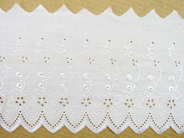 Flat white broderie anglaise fabric lace, 6 inches wide, with a pattern of small white flowers and dots, laid out on a flat surface.